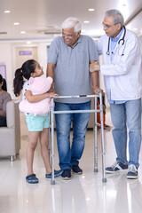 Granddaughter with male doctor teaching disabled grandfather to use walker at hospital
