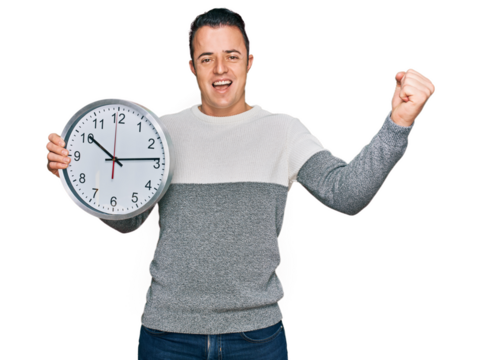 Handsome young man holding big clock screaming proud, celebrating victory and success very excited with raised arms