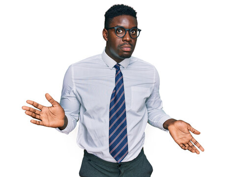 Handsome business black man wearing white shirt and tie clueless and confused expression with arms and hands raised. doubt concept.
