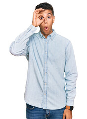 Young handsome african american man wearing casual clothes doing ok gesture shocked with surprised face, eye looking through fingers. unbelieving expression.