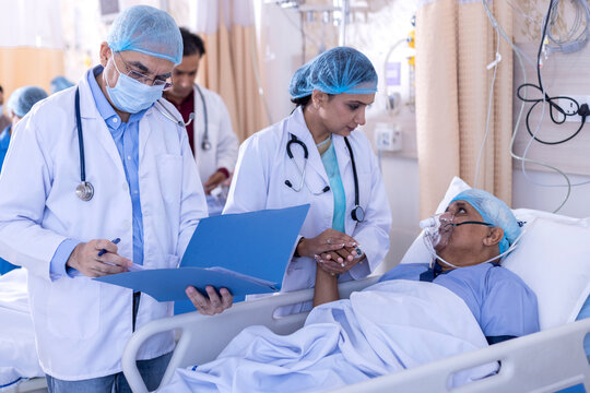 Two doctors writing report while treating patient in oxygen mask in hospital
