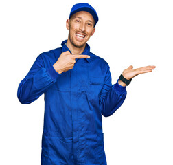 Bald man with beard wearing builder jumpsuit uniform amazed and smiling to the camera while...
