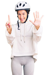 Beautiful brunette young woman wearing bike helmet and sporty clothes showing and pointing up with fingers number six while smiling confident and happy.