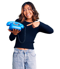 Young beautiful mixed race woman holding vintage telephone smiling happy pointing with hand and finger