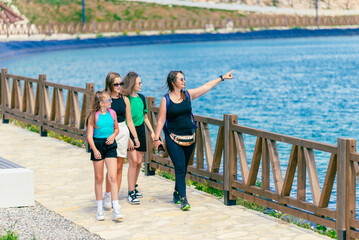Young girls and a woman are walking by the lake. Woman shows the girls a tourist attraction. Concept of mountain tourism and enjoyment