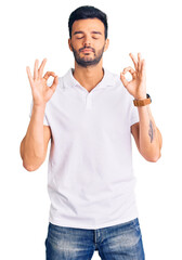 Young handsome hispanic man wearing casual clothes relaxed and smiling with eyes closed doing meditation gesture with fingers. yoga concept.
