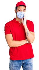 Young handsome hispanic man wearing delivery uniform and medical mask thinking looking tired and bored with depression problems with crossed arms.