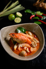 Tom Yum kung Spicy Thai soup with shrimp in a black bowl on a dark background