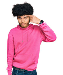Young african american man with afro hair wearing casual pink sweatshirt pointing unhappy to pimple...