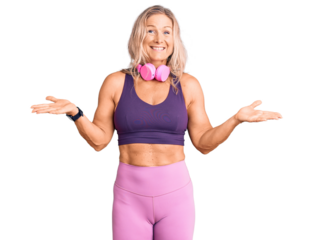 Middle age fit blonde woman wearing gym clothes and using headphones clueless and confused expression with arms and hands raised. doubt concept.