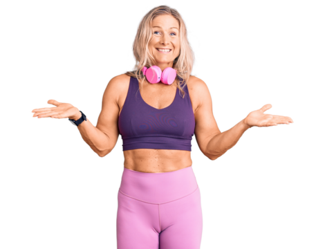 Middle age fit blonde woman wearing gym clothes and using headphones clueless and confused expression with arms and hands raised. doubt concept.