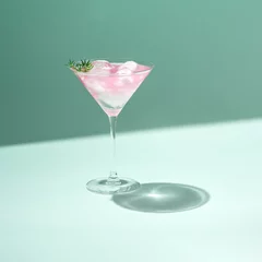 Foto op Plexiglas Tropical cold drink cocktail minimal concept with pastel pink martini glass and ice on green color background. Trendy sunlight summer party aesthetic. © Artemis Creative 