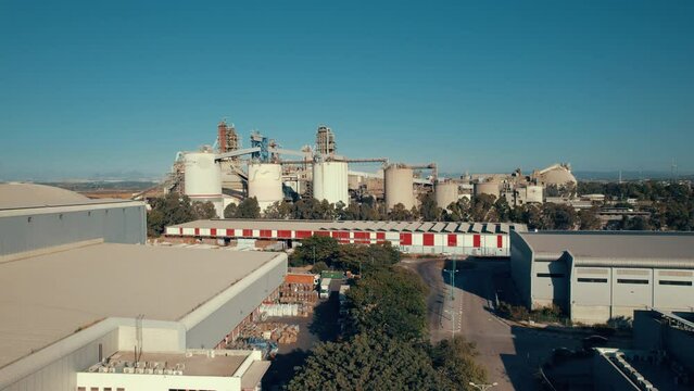 Aerial shot of a huge cement factory, an innovative industrial area with lots of hangars and trucks, a beautiful area with trees, push in shot
