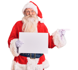 Old senior man with grey hair and long beard wearing santa claus costume holding banner smiling happy pointing with hand and finger to the side