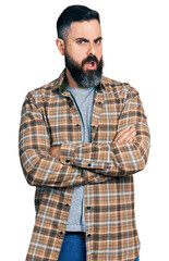 Hispanic man with beard with arms crossed gesture in shock face, looking skeptical and sarcastic, surprised with open mouth