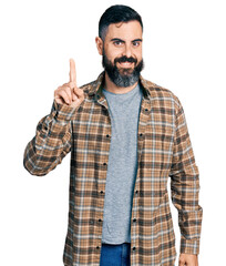 Hispanic man with beard wearing casual shirt showing and pointing up with finger number one while smiling confident and happy.