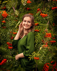 A girl in a green blouse stands in the park, in the garden near the mountain ash. The branches of the tree are located around her body.
Summer photo of a ripe mountain ash.