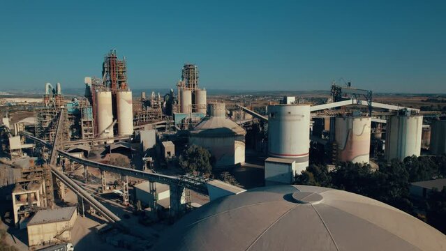 Aerial shot of a huge cement factory, innovative industrial area with lots of hangars and trucks, beautiful area with trees, parallax shot