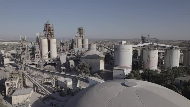 Aerial shot of a huge cement factory, innovative industrial area with lots of hangars and trucks, beautiful area with trees, parallax shot(D-LOG)