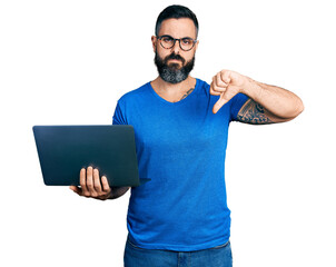 Hispanic man with beard working using computer laptop with angry face, negative sign showing...