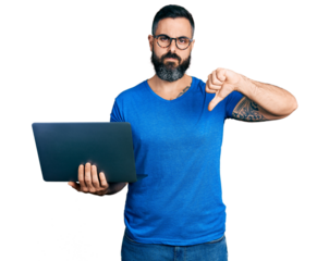 Hispanic man with beard working using computer laptop with angry face, negative sign showing dislike with thumbs down, rejection concept