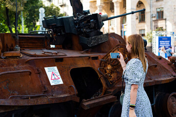 Naklejka premium girl takes a photo on the phone of a burnt Russian tank on the street of Kyiv, Ukraine. independence Day of Ukraine. 23.08.22