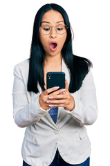Beautiful hispanic woman with nose piercing using smartphone typing message afraid and shocked with...
