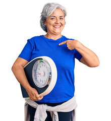 Senior woman with gray hair holding weight machine to balance weight loss pointing finger to one...