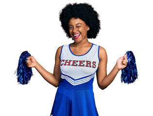 Young african american woman wearing cheerleader uniform using pompom winking looking at the camera...