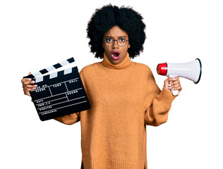 Young african american woman holding video film clapboard and megaphone afraid and shocked with...