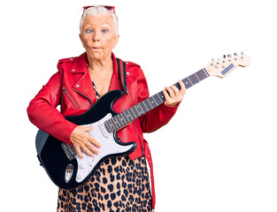 Senior beautiful woman with blue eyes and grey hair wearing a modern look playing electric guitar...