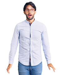 Fototapeta premium Handsome hispanic man wearing business shirt and glasses afraid and shocked with surprise and amazed expression, fear and excited face.