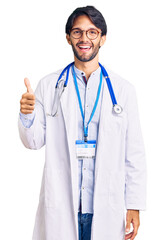 Fototapeta na wymiar Handsome hispanic man wearing doctor uniform and stethoscope smiling happy and positive, thumb up doing excellent and approval sign