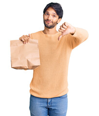 Handsome hispanic man holding take away paper bag with angry face, negative sign showing dislike...