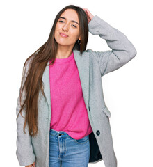 Young hispanic girl wearing business clothes confuse and wonder about question. uncertain with doubt, thinking with hand on head. pensive concept.