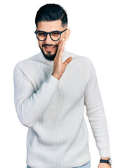 Young arab man with beard wearing elegant turtleneck sweater and glasses hand on mouth telling...