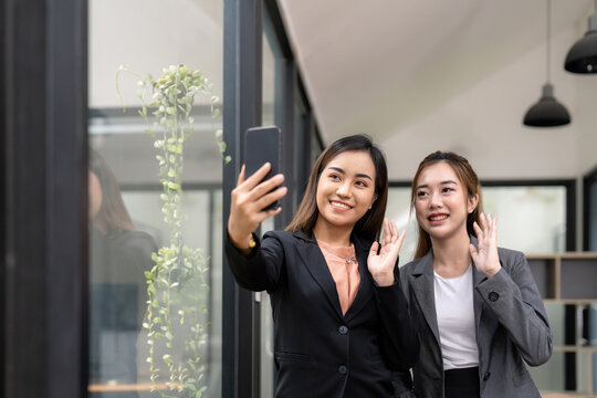 Two asian business woman waving hands to greeting partner during making video conference with her team.