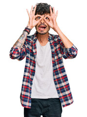 Young hispanic man wearing casual clothes doing ok gesture like binoculars sticking tongue out, eyes looking through fingers. crazy expression.