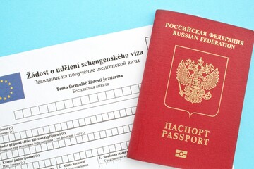 Schengen visa application form in Russian and Czech language and passport on blue background. Prohibition and suspension of visas for Russian tourists to travel to European Union and the Baltic States
