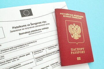 Schengen visa application form in Russian and Latvian language and passport on blue background. Prohibition and suspension of visas for Russian tourists to travel to Europe Union and Baltic States