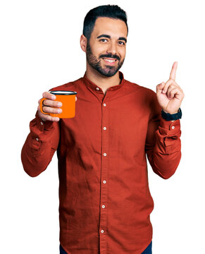 Young hispanic man with beard drinking a cup of coffee smiling happy pointing with hand and finger to the side