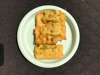 Tempe Goreng is an Indonesian food made from fermented soybeans and then fried using flour. Photographed on a green plastic plate isolated on a dark background