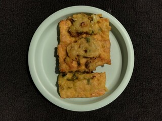 Tempe Goreng is an Indonesian food made from fermented soybeans and then fried using flour. Photographed on a green plastic plate isolated on a dark background