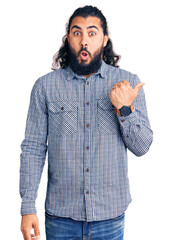 Young arab man wearing casual clothes surprised pointing with hand finger to the side, open mouth amazed expression.