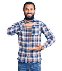 Fototapeta premium Young arab man wearing casual clothes gesturing with hands showing big and large size sign, measure symbol. smiling looking at the camera. measuring concept.
