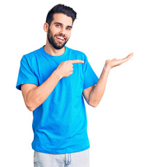Young handsome man with beard wearing casual t-shirt amazed and smiling to the camera while presenting with hand and pointing with finger.