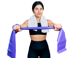 Young brunette woman with blue eyes training arm resistance with elastic arm bands smiling looking to the side and staring away thinking.