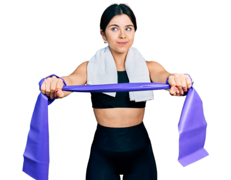 Young brunette woman with blue eyes training arm resistance with elastic arm bands smiling looking to the side and staring away thinking.