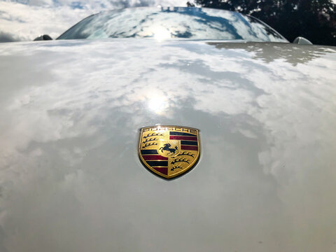 Logo Porsche sur un capot blanc avec des reflets
