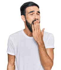 Young hispanic man wearing casual white t shirt bored yawning tired covering mouth with hand. restless and sleepiness.